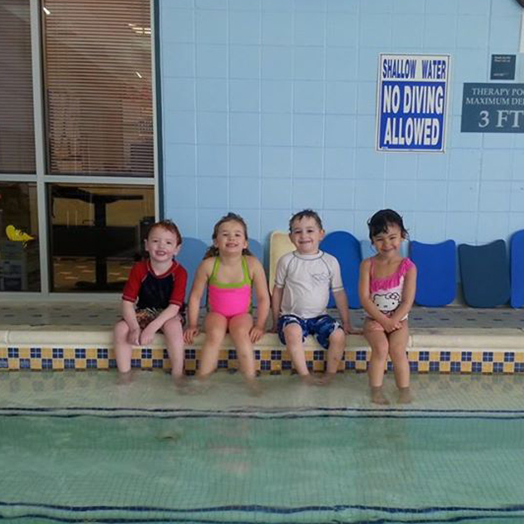 Four kids dangling their feet in the pool