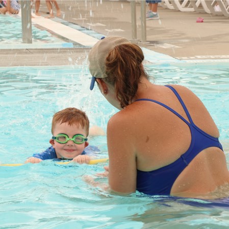 Swim instructor coaches a young boy in the water.