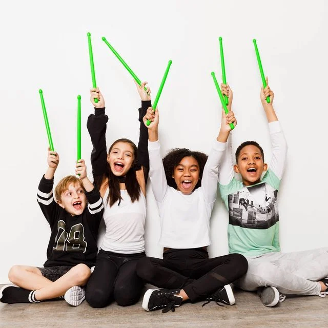 Boys and girls holding green drumsticks in the air