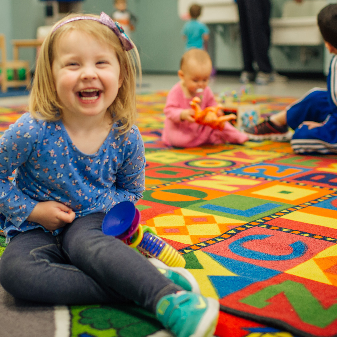 Toddler girl wearing a blue shirt and headband, laughing