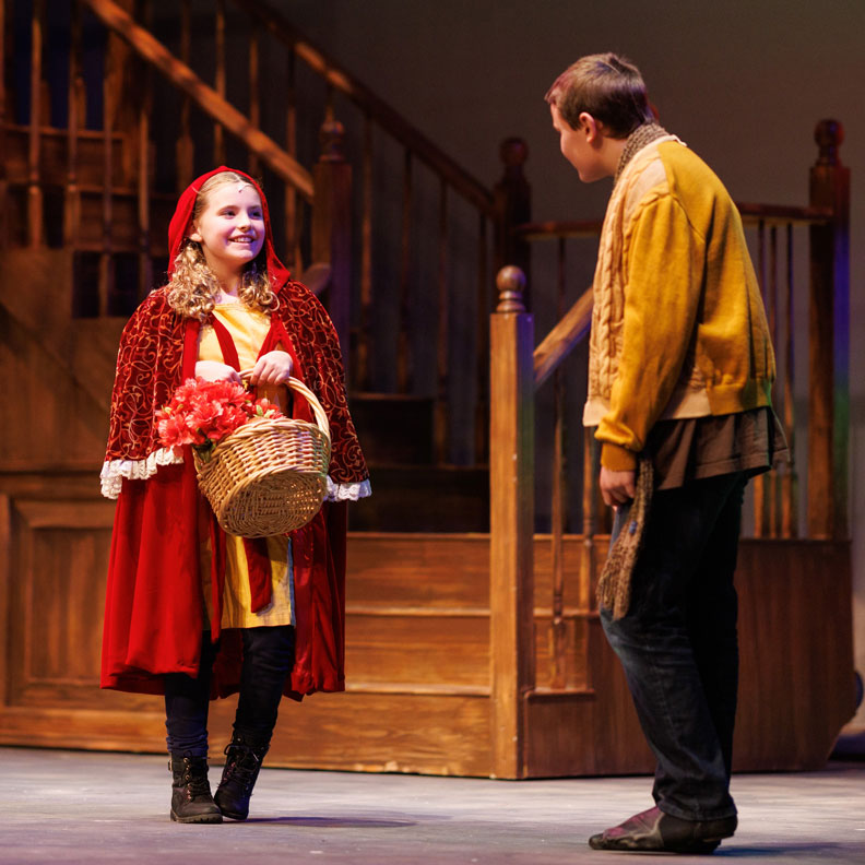 Girl playing Little Red Riding Hood smiling at The Baker