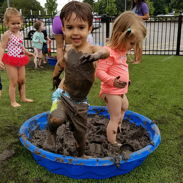 A little boy and girl are standing in a baby pool full of mud.