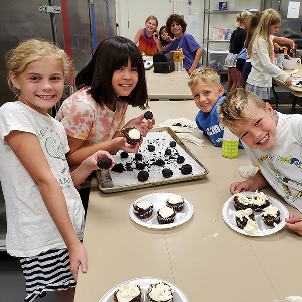 Four children are standing around a table icing cupcakes.