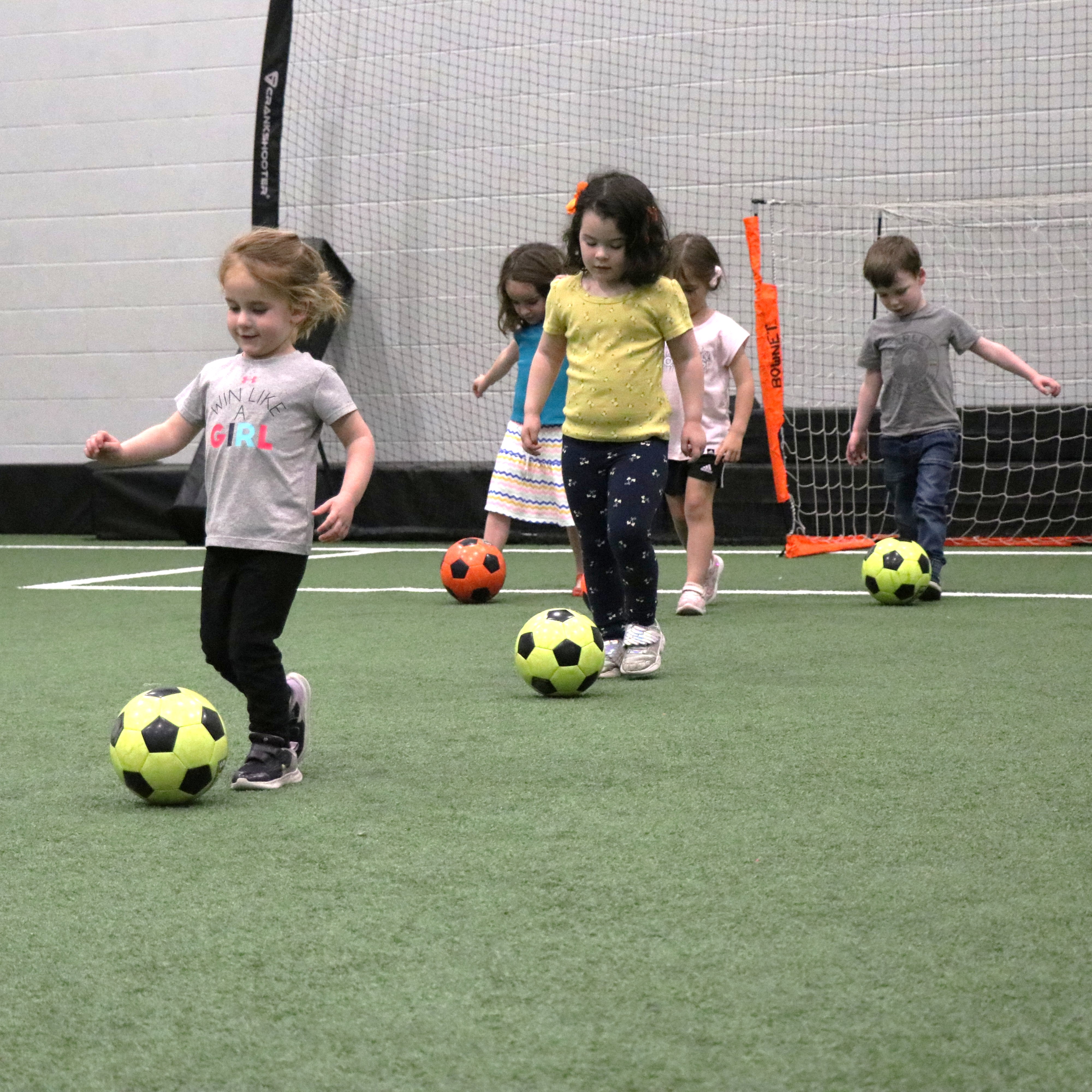 Two girls with soccer balls dribbling them on the field