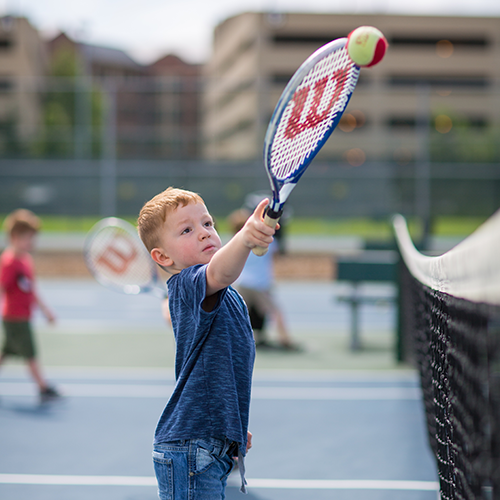 Boy reaching for a tennis ball with his racquet.
