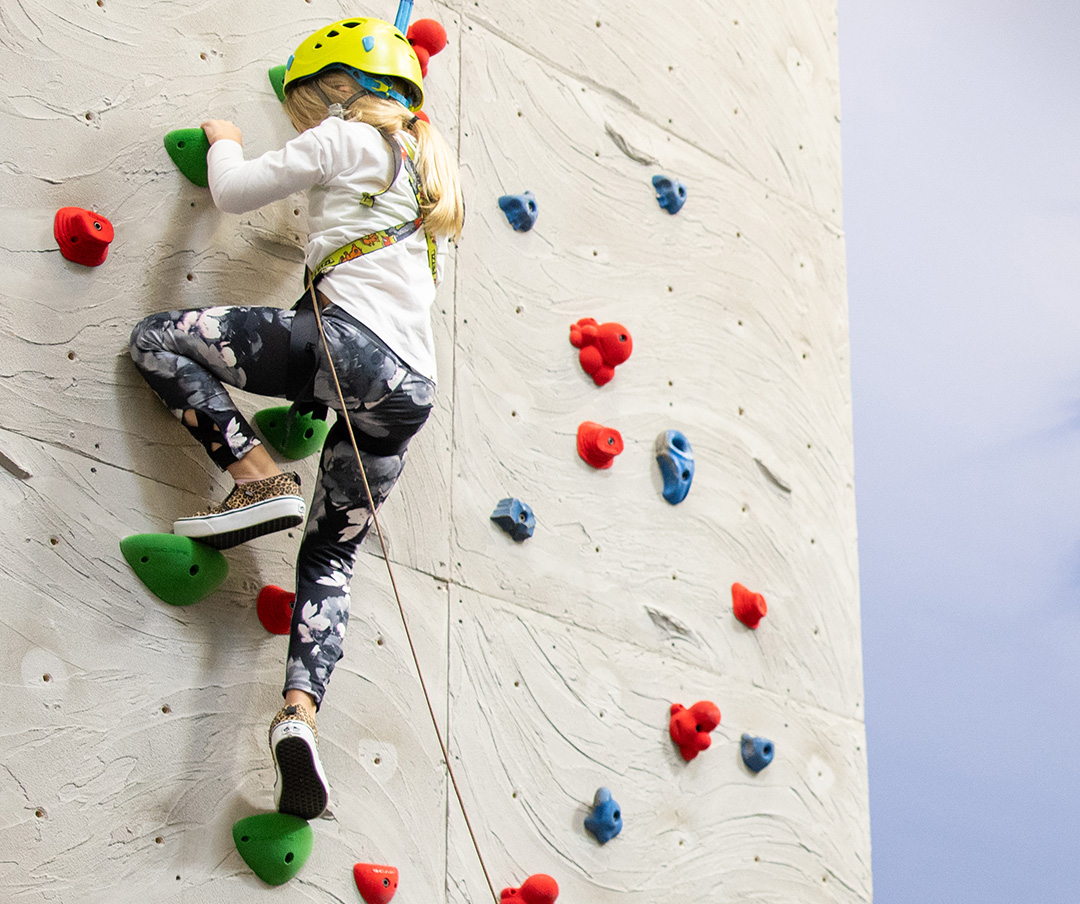 girl climbing a rock wall in the Big J Clubhouse