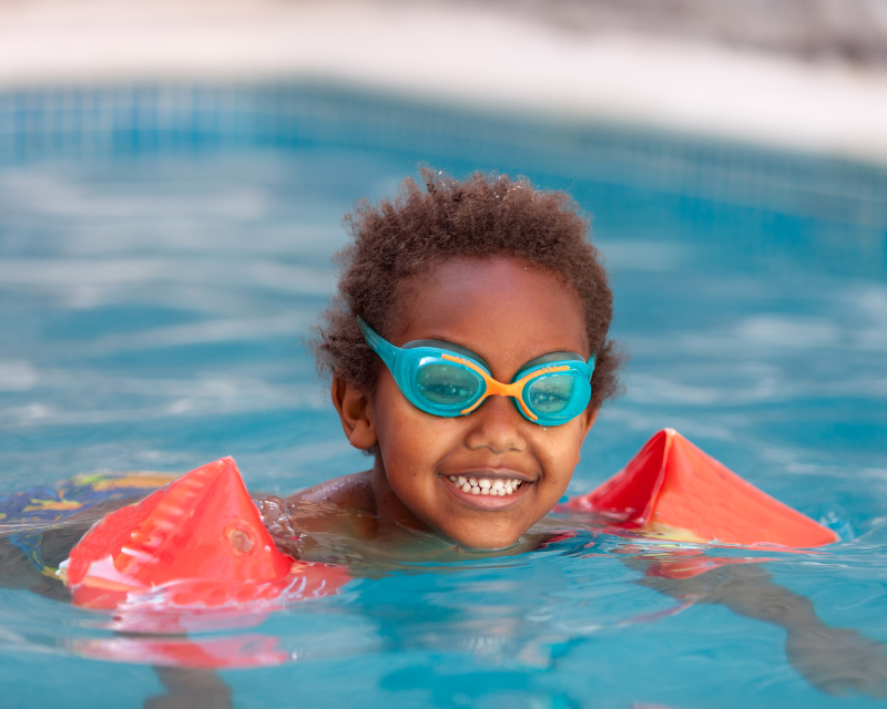 Young boy swimming in pool with goggles and arm floats