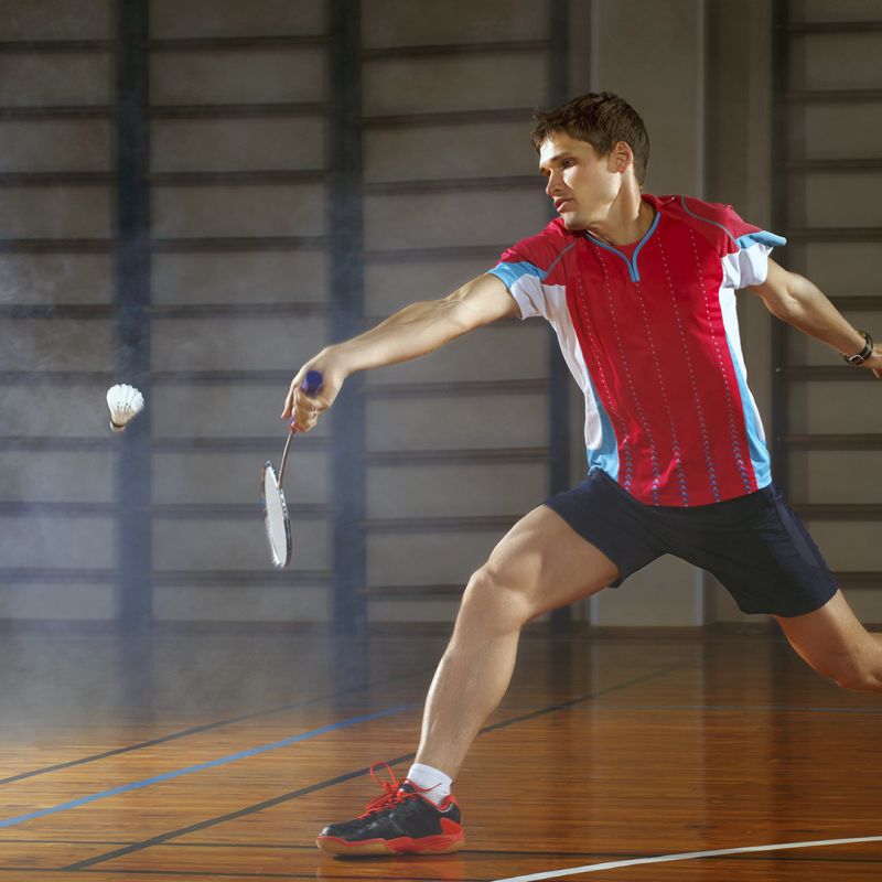 Man in red shirt lunging for shuttlecock