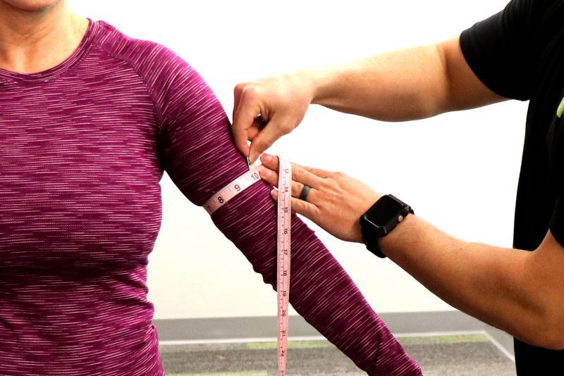 Trainer measuring client's arm with tape measure