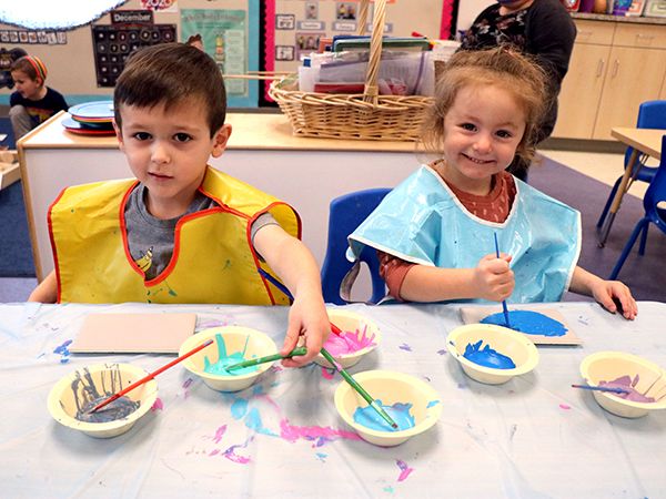 Two preschoolers painting with smocks on.