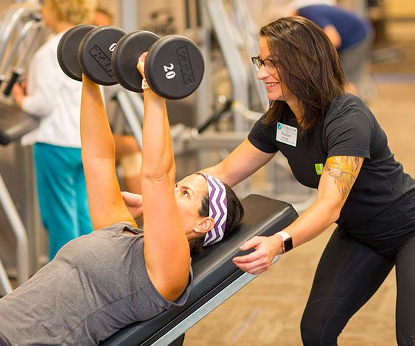 Personal trainer helps J member safely lift dumbbells